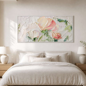 White framed horizontal flowers above a cream upholstered bed between matching lamps.