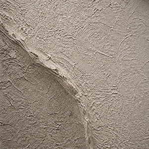 Close-up of rough sand, taupe, and ivory sculpted surface texture.