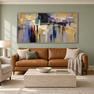 Hand-painted textured abstract wall art in golden ochre, smoky violet, slate blue, and charcoal, displayed in a living room in a silver frame.