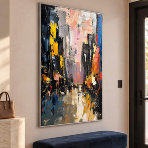 Textured rainy city street painting with yellow lights and dark buildings in a silver frame in an entrance hall.