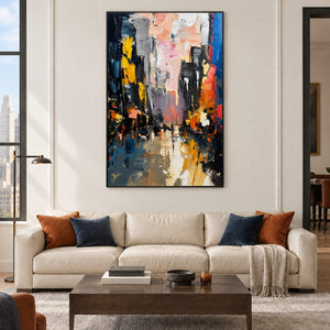 Textured rainy city street painting with yellow lights and dark buildings in a black frame in a living room.
