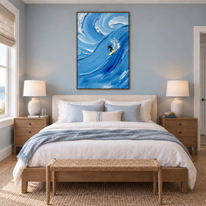 Riding the Wave in a wood frame above a cream bed with pale blue linen and a woven bench.