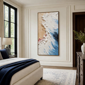 Wood-framed blue and white textured artwork beside a cream bed with deep blue bedding accents.
