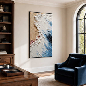 Black-framed coastal abstract artwork beside wooden bookshelves, a desk, and a deep blue armchair.