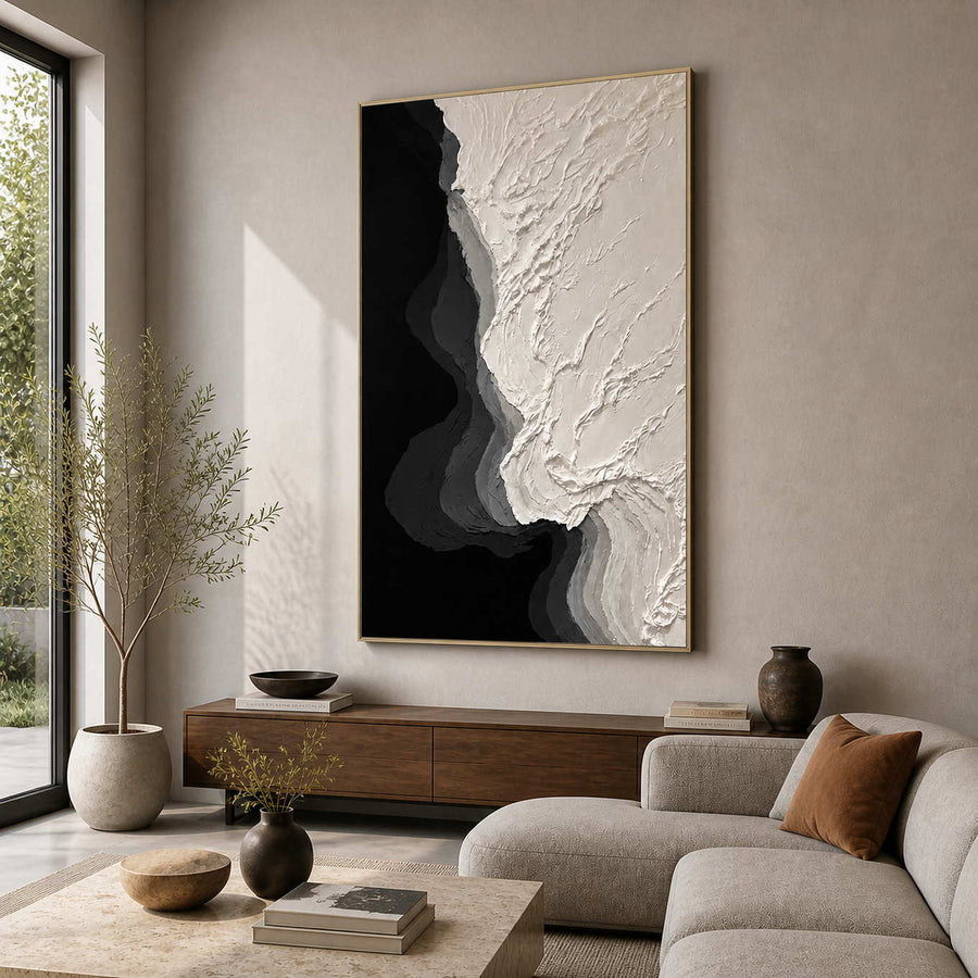 Gold framed ivory and black textured painting beside a living room sofa.