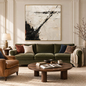 Ivory abstract painting with sweeping black marks and fine crossing lines in a gold frame in a living room.