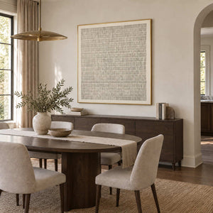 Slow and Lasting in a gold frame above a sideboard beside a dark oval dining table and cream chairs.