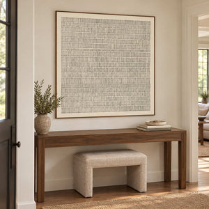 Slow and Lasting in a wood frame above a dark hallway console with a leafy vase and a cream stool below.