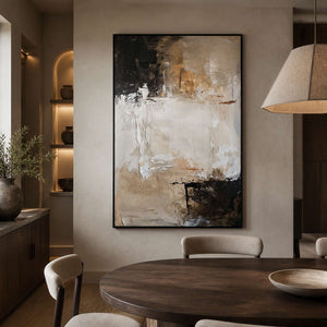 Black framed beige abstract painting displayed beside a dining table.
