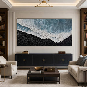 Black framed coastal artwork between bookcases above a dark study lounge cabinet.