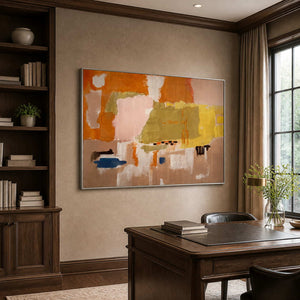 Silver framed colorful abstract artwork beside wooden bookshelves above a home office desk.
