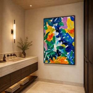 Black framed colorful floral artwork beside a stone vanity in a warmly lit bathroom.