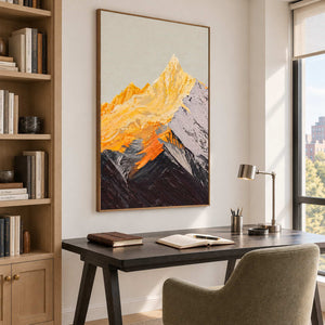 Angled view of golden and gray mountain artwork in a brown wood-look frame above a study desk beside a bookshelf.