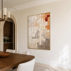 Gold-framed textured abstract wall art beside a wooden dining table and cream upholstered chairs.