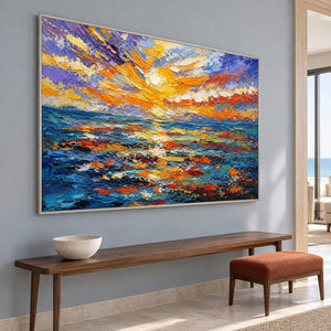 Textured seascape painting with a gold and orange sunset over blue water in a silver frame in an entrance hall.