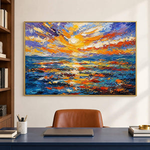 Textured seascape painting with a gold and orange sunset over blue water in a gold frame in a home office.