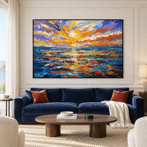 Textured seascape painting with a gold and orange sunset over blue water in a black frame in a living room.