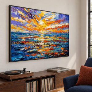 Textured seascape painting with a gold and orange sunset over blue water in a black frame in a lounge.