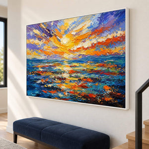 Textured seascape painting with a gold and orange sunset over blue water in a white frame on a stair landing.