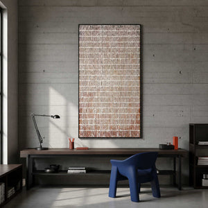 Black framed white grid painting over a desk in a concrete walled study.