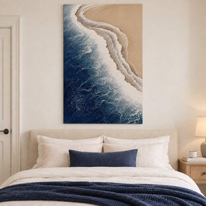 White surf curling along a sandy shore beside dark blue water without an outer frame, displayed above a bed.