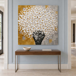 White flowers and black vase painting above a slim wood console on a blue-gray wall.