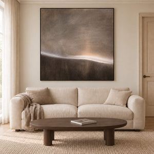 A thin glowing horizon between smoky gray and dark brown fields in a black frame, displayed above a sofa in a living room.