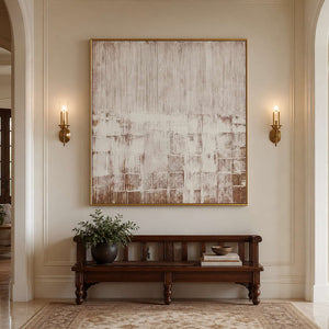 Gold framed cream and brown abstract artwork above a wooden bench in a hallway.