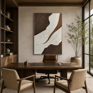 Silver-framed abstract wall art behind a wooden office desk beside a tall window.