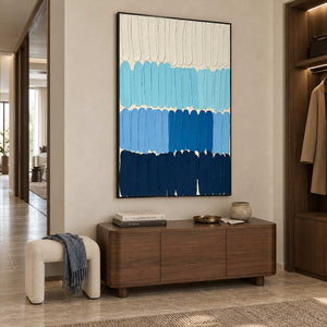 The Sea's Rhythm in a black frame above a wood sideboard beside a cream bench in an entryway.