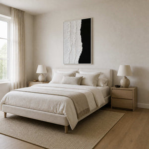 White framed textured artwork above a cream bed between matching lamps and oak nightstands.