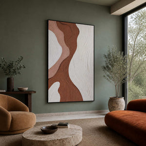 Brown and blush abstract artwork in black frame beside caramel lounge chairs.