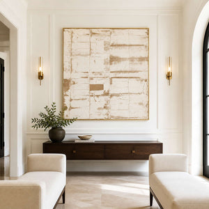 Gold-framed pale abstract above a floating wooden console between slim entrance hall sconces.
