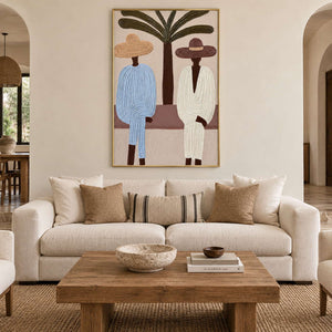 Palm and seated figures artwork above a cream sofa with striped and neutral cushions.