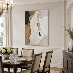 Gold framed earthy textured artwork above a dining table set with plates and white flowers.