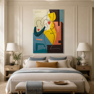White-framed figurative artwork above a cream bed with blue and ochre cushions between matching bedside lamps.