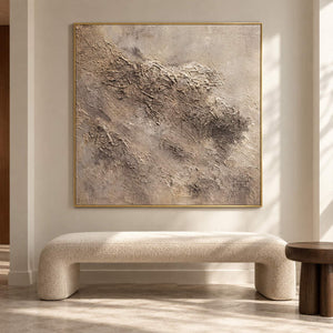 In a seating area, an artwork with a gold-colored frame shows irregular beige and taupe relief-like textures on a pale square ground.