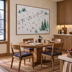 Snowy ski slope painting with red chairlifts, colorful skiers, and evergreen trees in a brown wood frame in a breakfast dining area.