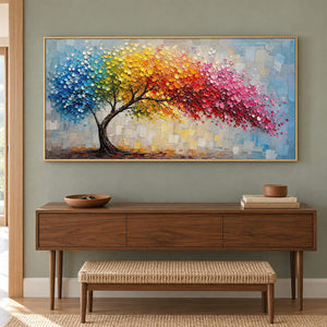 Rainbow tree painting with raised colorful leaves and a pale blue background in a gold frame in an entryway.