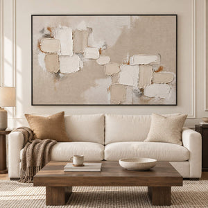 Textured abstract painting with raised ivory and taupe blocks in a black frame in a living room.