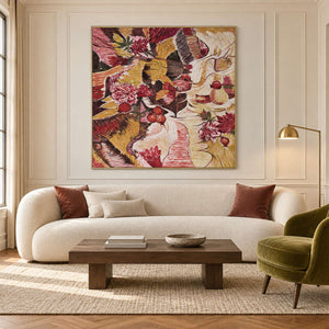 In a living room above seating, an artwork with a gold-colored frame shows red flowers and rounded fruit forms woven through ochre, cream and dark bands.