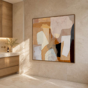 Softly colored abstract artwork beside a wooden bathroom cabinet on a beige wall.