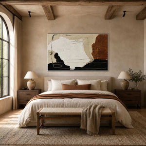 White-framed earthy abstract artwork above a neutral bed beneath exposed wood ceiling beams.