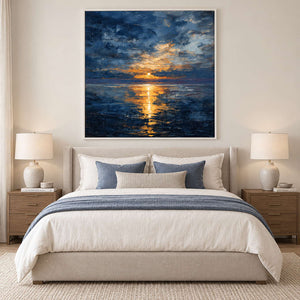 White-framed seascape above a neutral upholstered bed with blue cushions and a blue throw.