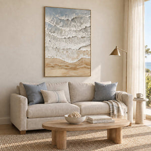 Whispering Tides in a gold frame above a cream sofa with blue-gray cushions beside a sunny window.