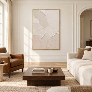 Hand-painted ivory abstract canvas with overlapping raised organic forms, displayed in a living room in a gold frame.