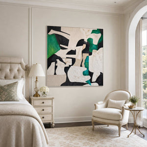 White framed green abstract artwork beside a cream bed and upholstered bedroom chair.