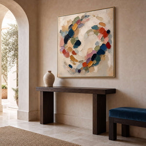 Square multicolor wall art above a sculptural console in a warm entryway.