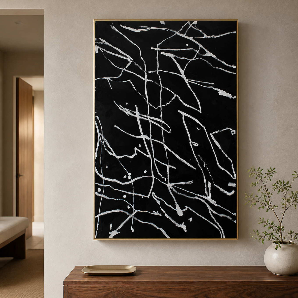 Gold framed black and white line painting above a wooden entryway console.