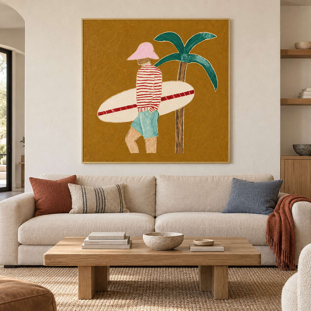 Ochre surfer painting above a cream sofa with rust, striped, and blue cushions.